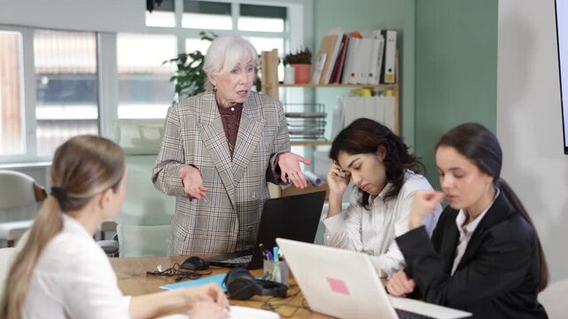 Angry mature woman standing and scolding colleagues during a stressful corporate meeting in office. High quality 4k footage