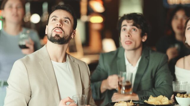 Sports fans react with delight to changes in lucky game. Group of friends hangs out at sports bar, watching teams match, and following progress of game. Video broadcast of match or race is available.