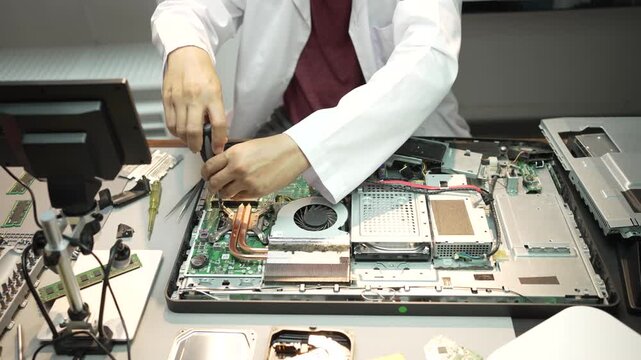 Technician in a white coat repairing an open laptop motherboard at a workbench with tools, close-up view of computer maintenance, electronics service and hardware fixing