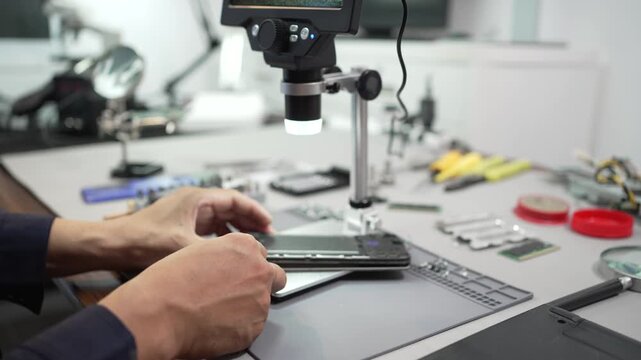 Technician repairs a laptop at a workbench using a screwdriver, with tools and electronic parts spread across the table in a clean workshop