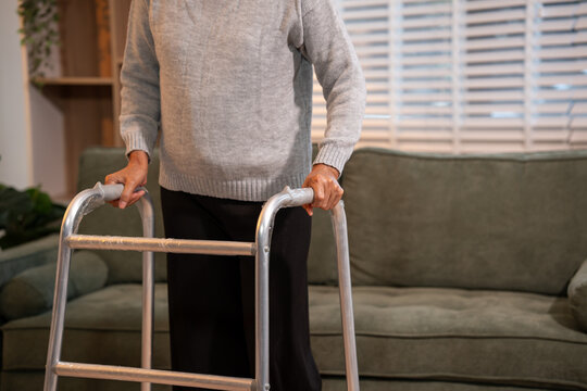 Senior adult using a walking frame at home in a living room, showing daily mobility support, recovery, safety and independent aging indoors.