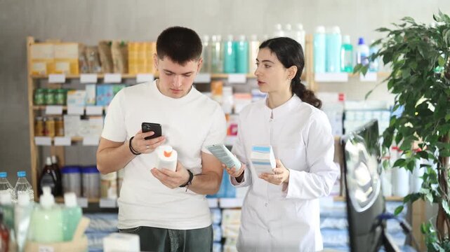Guy in pharmacy scans QR code on emollient cream and uses link to go to manufacturers website. Client learns information about product, reviews and recommendations for use. Pharmacist offer help and