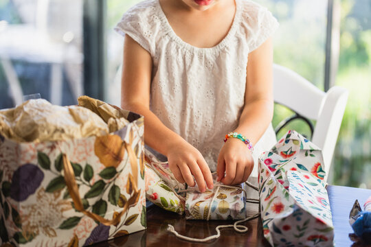 Excited child opening gifts wrapped in pretty paper at her birthday party inside home