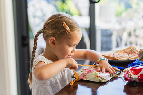 Excited child opening gifts wrapped in floral paper at her birthday party inside home