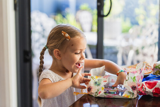 Excited child opening gifts wrapped in floral paper at her birthday party inside home