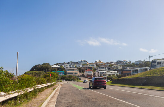 Coastal houses on hillside seen from road with car traveling through city