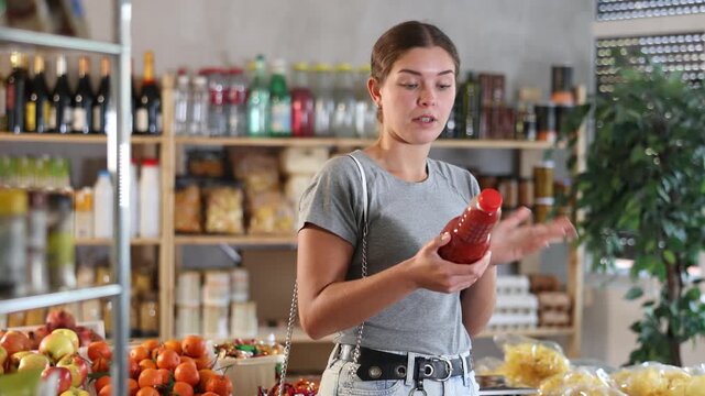 Young woman chooses natural vegetable juice in a supermarket. Customer holds bottle of tomato juice in her hand. High quality 4k footage