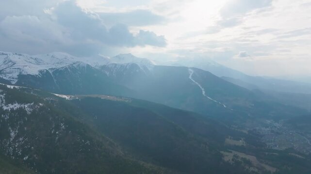 Drone flies sideways past snowy Rodnei peaks above valleys and forests Romania