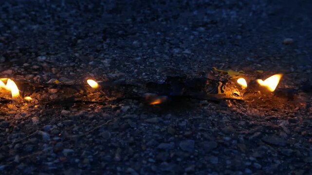Line of fire burning along a fuse or flammable material on dark asphalt at night, with bright yellow flames illuminating the ground in a close up shot of a dangerous combustion concept