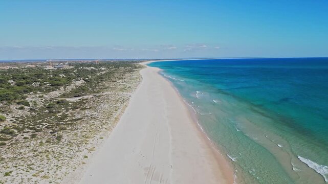 Aerial view moves along empty sandy beach and turquoise sea with coastline vegetation