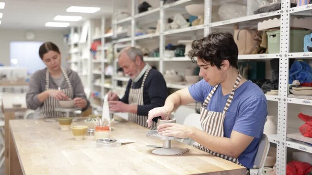 Young woman, young man and elderly man in ceramic workshop sculpting clay products during master class