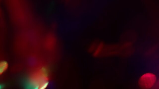 Real small multi-color rainbow bokeh dots in green and red scatter randomly across the center of the black surface. Organic optical light leak for nightclub visuals, party events, and DJ content.