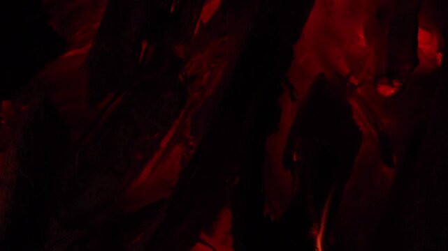 Close-up of glowing red embers and charred firewood inside a burning fire. The intense red glow and dark textures create a dramatic background representing heat, energy, and combustion.