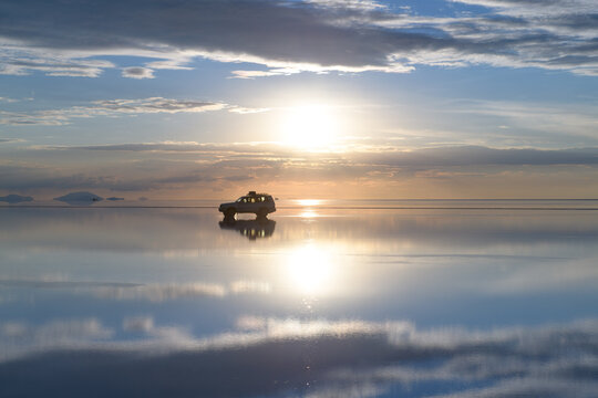 Serene car reflection on uyuni salt flat with water during sunset in bolivia