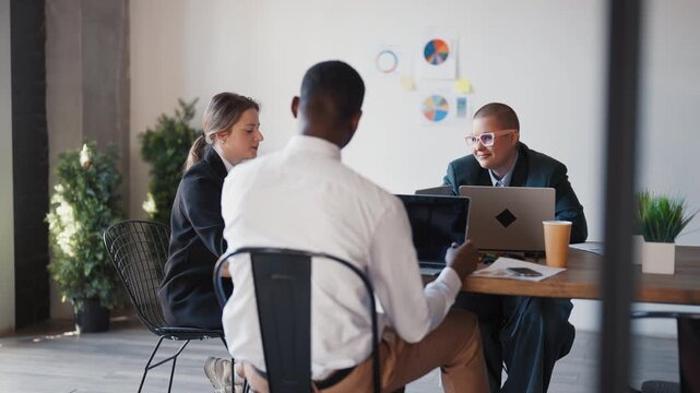 Young adult people working in office, male and female colleagues in co-working. Diverse office workers talking about work sitting at table in conference room, marketing and financial professionals