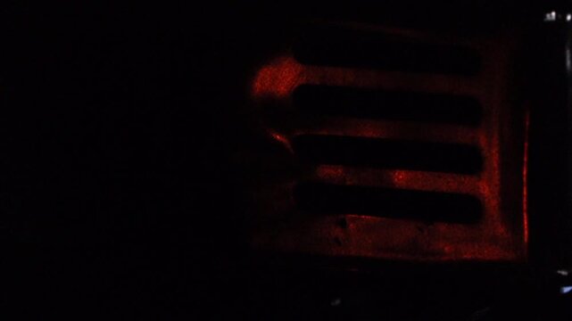 Close-up view of a glowing electric heater grille emitting a deep red-orange light in a dark indoor setting. The image highlights warmth, heating technology, energy use, and winter comfort,