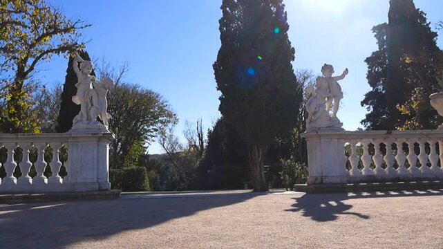 Picturesque view of the manicured gardens at the historic Queluz National Palace, featuring rococo statues on a sunny day with distinct shadows and subtle lens flare from the bright sun