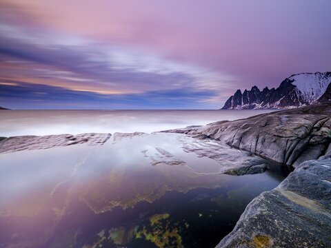 Natural pool on granite beach, Devils Teeth mountain peak in the back, Okshornan mountain range, Tungeneset, Senja Island, Troms, Norway