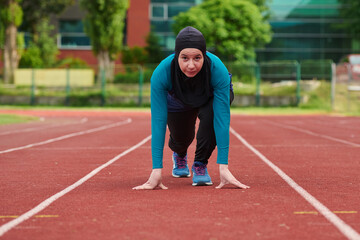 Obraz premium Female Hijab Runner On Track Starting Sprint Pose Showing Determination Fitness And Athletic Focus