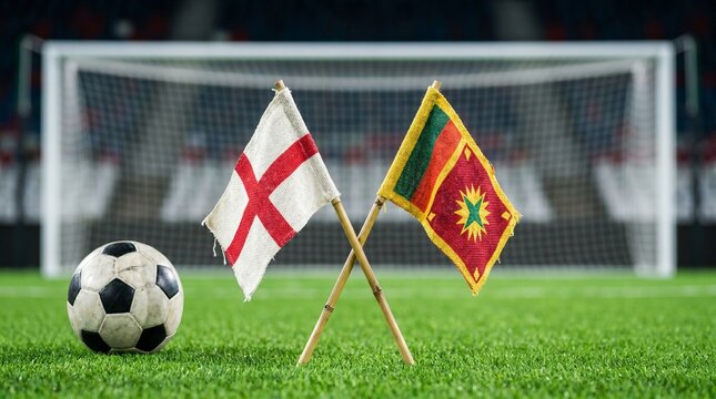 Soccer ball sits beside two crossed national flags on a lush green field before a stadium goal.