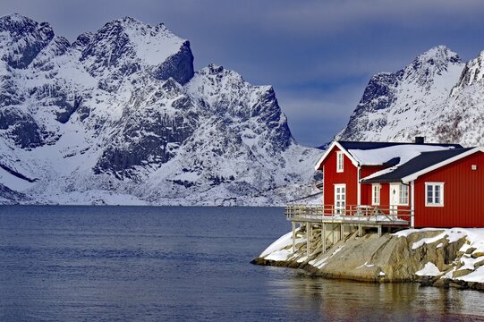 Red house by the fjord in front of snow-covered mountains in a wintry landscape, Scandinavian style with wooden structure, Rorbuer, holiday, Hamn&ouml;y, Lofoten, Nordland, Norway