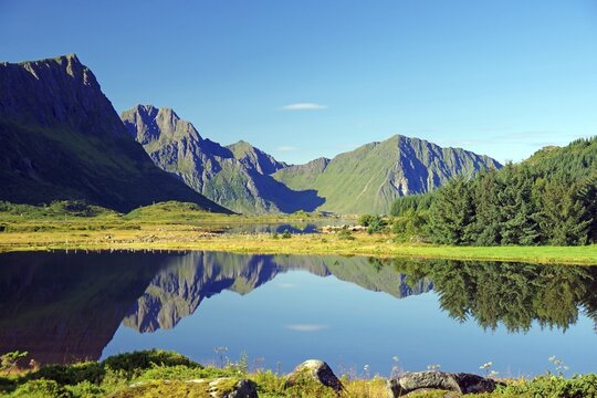 Mountains are reflected in a calm lake under a cloudless sky, Leknes, Vestv&aring;g&oslash;ya, Lofoten, Nordland, Norway