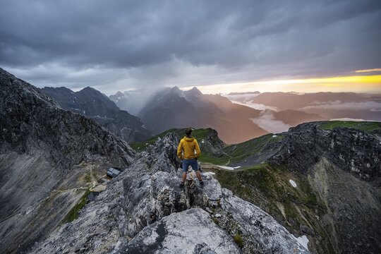 Hikers at the summit of the Westliche T&ouml;rlspitze, in the background cloudy mountains at sunset with dramatic light, view of Frauenalpl, Wetterstein Mountains, Garmisch Partenkirchen, Bavaria, Germany