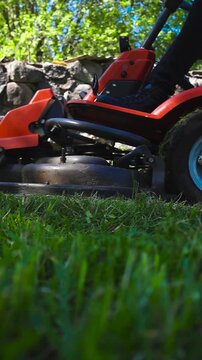 Close up low angle view of a red riding lawn mower cutting tall green grass in a sunny backyard, showcasing garden maintenance with a powerful grass cutting machine on a beautiful summer day
