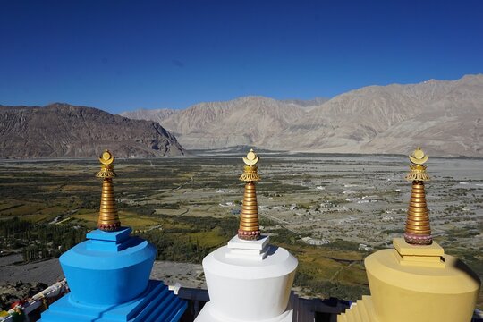 Three colorful traditional Buddhist stupas with a beautiful mountain valley in the background