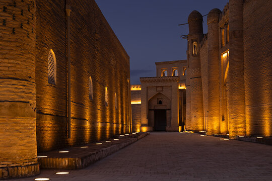 Illuminated brick walls and gateway of Ichan Kala old town in Khiva at twilight. Warm ground lights highlight the ancient fortress architecture against a deep blue evening sky. Ideal for travel.