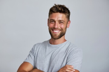 Obraz premium The smiling man in a gray t-shirt with folded arms studio portrait