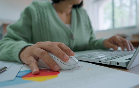 Close up hand's woman using wireless computer mouse working online on laptop computer at office desk.