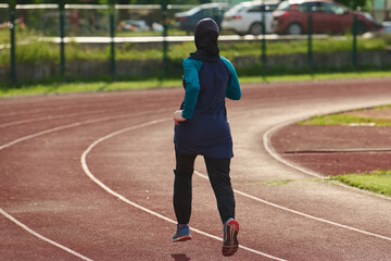 Obraz premium Woman in Hijab Running on Outdoor Track for Fitness and Training in Modest Sportswear