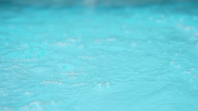 Rhythmic blue water bubbling with oxygen in a pool, turquoise liquid surface moving with soothing waves and calming ripples creating a peaceful and refreshing background