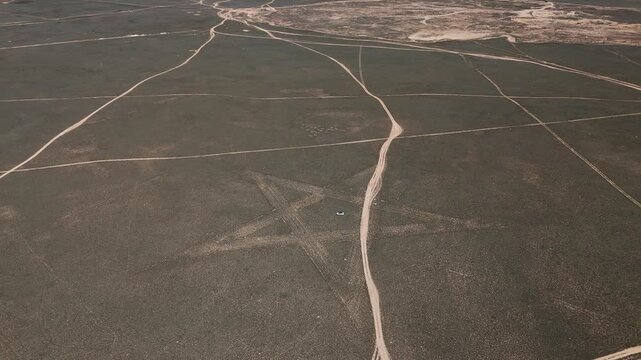 A stunning, large-scale aerial drone shot from Mangystau, Kazakhstan. A massive star-shaped geoglyph is carved into the arid desert ground. In the exact center of this gigantic symbol sits 