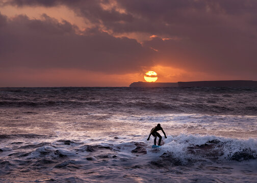 Silhouette man surfing on sea against cloudy sky at sunset, Pembrokeshire, Wales, UK