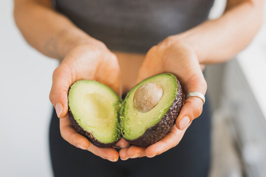 Hands of woman holding halved avocado
