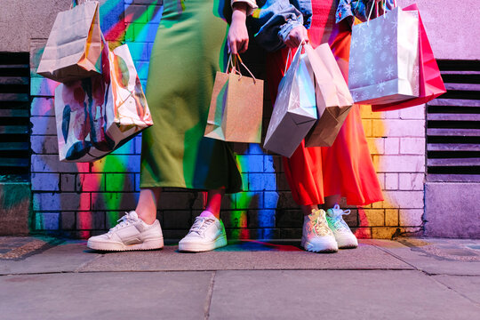 Lesbian friends holding shopping bags in front of brick wall
