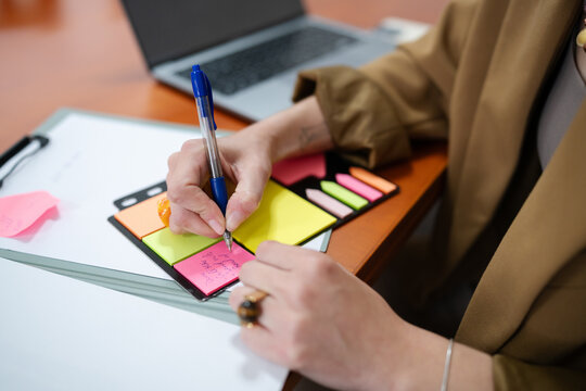 Hand writing on a colorful sticky note at a home workspace