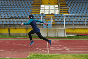 Obraz premium Young Female Hijab Runner Sprinting on Outdoor Track in Empty Stadium Training for Competition