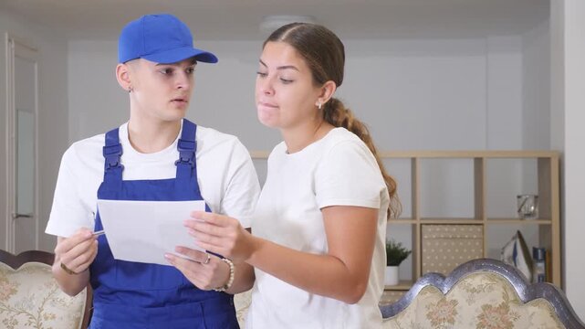Master in uniform with documents in his hands discusses with the young landlady of the apartment the plan of repair work, making important notes on paper.. High quality 4k footage