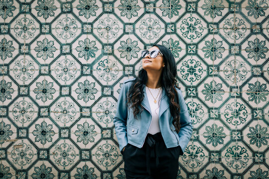 Portrait of young woman wearing light blue leather jacket and sunglasses in front of Azulejo wall, Lisbon, Portugal