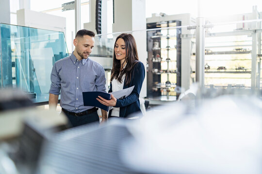 Smiling businessman and businesswoman looking at folder in modern factory