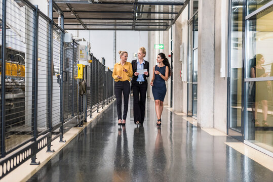 Three women with tablet walking and talking in factory shop floor