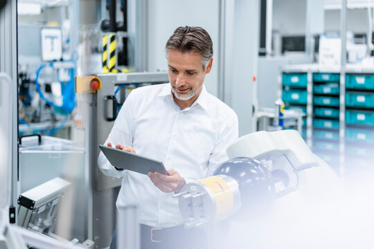 Businessman with tablet at assembly robot in a factory