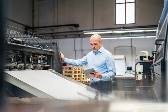 Businessman with tablet examining machine in a factory