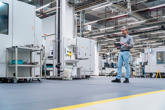 Engineer using tablet in modern production hall with machinery