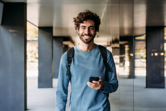 Happy man with smart phone standing in corridor