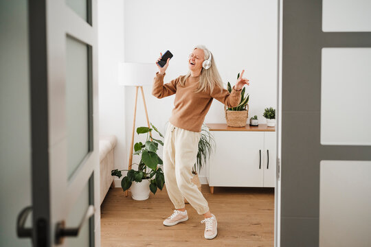 Cheerful mature woman wearing wireless headphones dancing at home