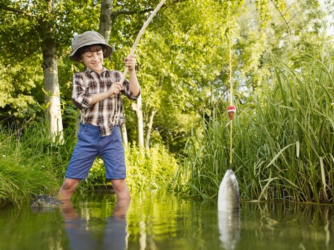 Boy fishing with a wooden rod and catching a fish in a stream